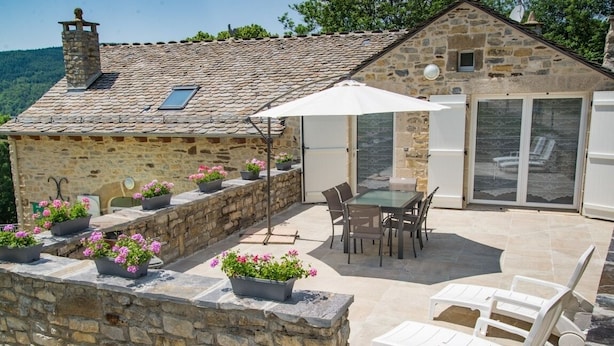 A stone building with a tiled roof, outdoor seating area with a table and chairs, and potted plants.