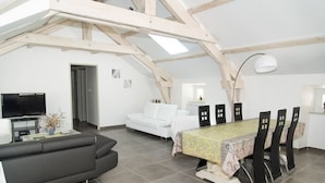 A modern loft-style living space with a dining area, a sofa, a TV, and a skylight.