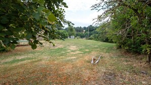 An open grassy area with trees and a stone wall in the background. - Gîtes de France 11 people in Le Teil (ALBARET LE COMTAL)