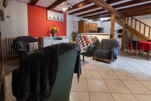 A cozy living room with a fireplace, a dining area with a red table, and a kitchen with wooden cabinets.