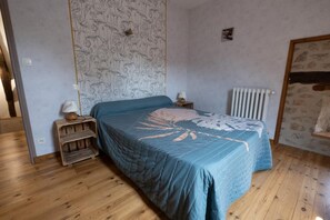 Un dormitorio con cama, mesitas de noche de madera, un radiador y un papel tapiz estampado.