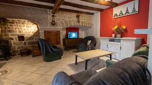 A cozy living room with stone walls, a fireplace, a television, and a red wall with Eiffel Tower artwork. - Gîtes de France 11 people in Le Teil (ALBARET LE COMTAL)
