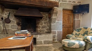 A stone fireplace with a television mounted on the wall, a wooden table with books, and a patterned armchair.