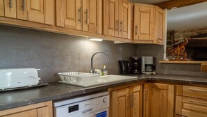 A kitchen with wooden cabinets, a white dishwasher, a coffee maker, and a stone wall in the background.