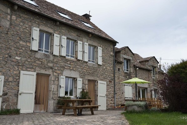 A stone building with multiple windows and doors, a wooden bench, and a green umbrella.