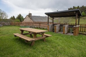 A picnic area with a wooden table and benches, a stone wall, and a fenced garden.