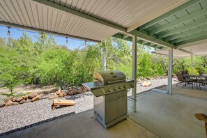 Un patio exterior con una parrilla, zona de estar y vistas a árboles.