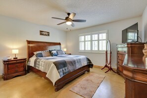 Un dormitorio con cama de madera, mesita de noche, cómoda, ventilador de techo y ventana con persianas.