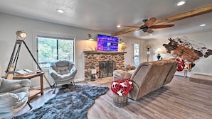 A modern living room with a stone fireplace, leather sofas, a large TV, and a ceiling fan.