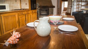 Una mesa de comedor de madera con platos, una jarrón y un vaso. Se observa un microondas y armarios de madera al fondo.
