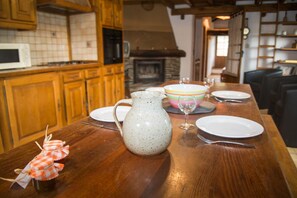 A wooden dining table set with plates, a pitcher, and a glass. A microwave and wooden cabinets are in the background.