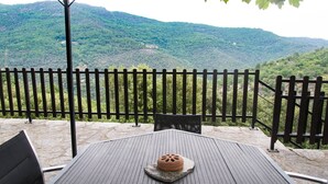 Un espacio al aire libre con mesas y sillas, una valla de madera y vistas a una cadena montañosa boscosa.