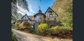 A Tudor-style house with a stone tower, surrounded by lush greenery and a paved driveway. - Captivating and Unique Tudor Inspired "Gingerbread house" (Kallista)