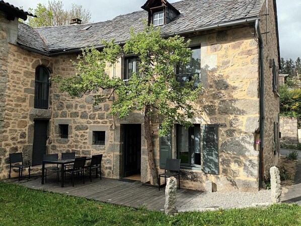 A stone building with a wooden deck, outdoor seating, and a tree in front.