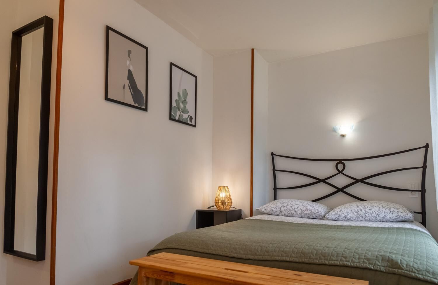 A bedroom with a bed, a bedside table with a lamp, and two framed pictures on the wall.