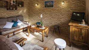 Un salon chaleureux avec un mur en pierre, un canapé agrémenté de coussins, une table basse en bois et un téléviseur posé sur un meuble en bois.