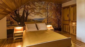 Une chambre à coucher avec un lit en bois, deux tables de chevet et une grande fresque représentant un arbre et un paysage sur le mur.