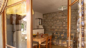 A dining area with a stone wall, a table with chairs, and a ceiling light fixture. - Gîte "Le Noyer" 4 pers in Blajoux (BLAJOUX)