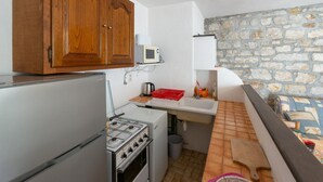 A compact kitchen with wooden cabinets, a gas stove, a microwave, and a stone wall. - Gîte "Le Noyer" 4 pers in Blajoux (BLAJOUX)