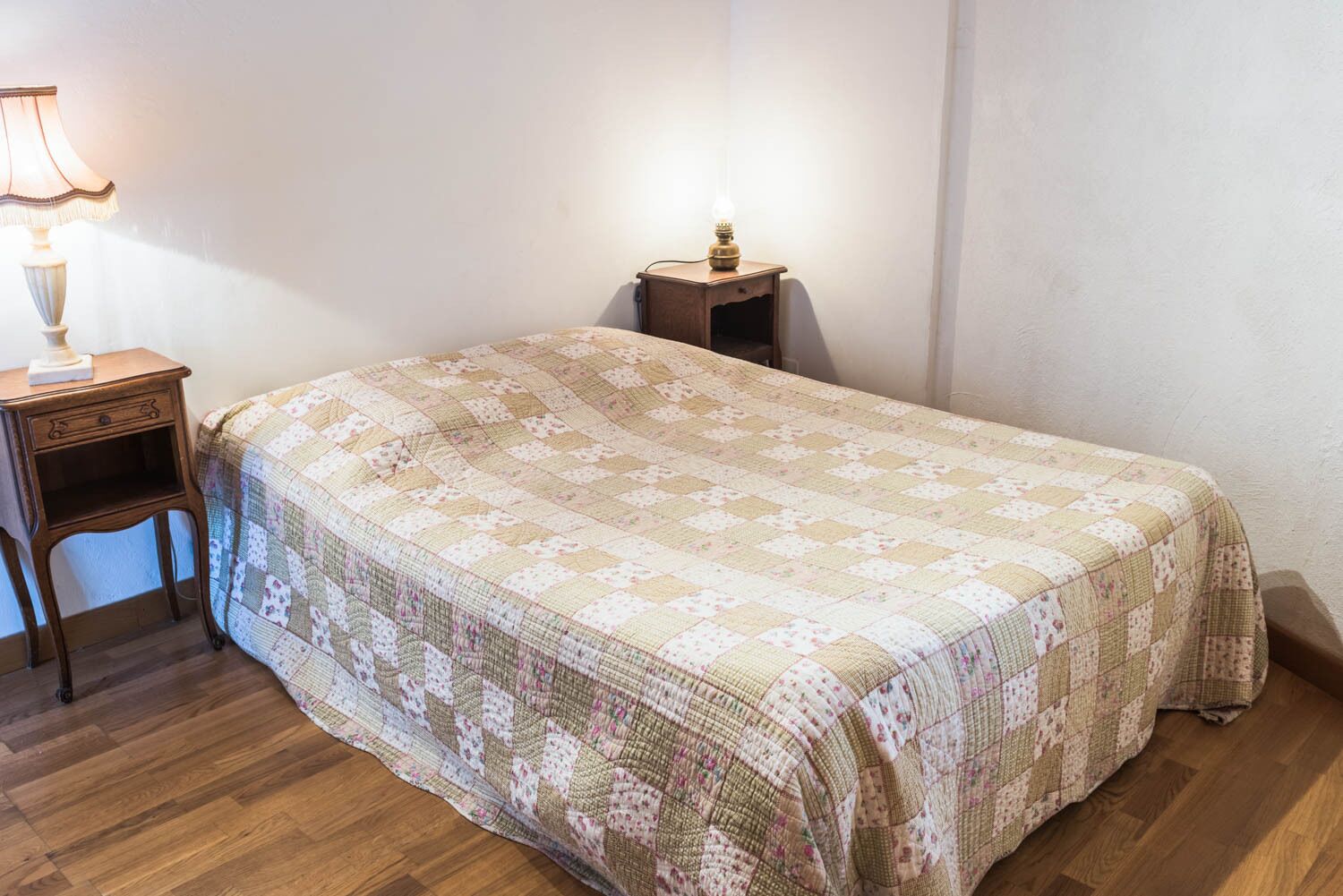 Una camera da letto con un letto, un comodino, una lampada e un pavimento in legno.
