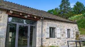 A stone building with a large glass door and shutters, a metal roof, and a sign indicating "La Grange". - Lzg090a - Gîtes de France 3 Épis 6 Pers à Coulagnettes (SAINT-AMANS)