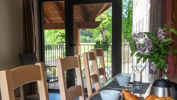 A dining area with wooden chairs, a table set with white bowls, glasses, and a basket of croissants. - Lzg090a - Gîtes de France 3 Épis 6 Pers à Coulagnettes (SAINT-AMANS)