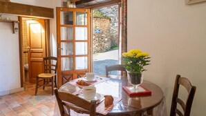 A dining area with a round table, chairs, a vase of yellow flowers, a croissant, and a cup of coffee.