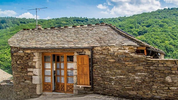A stone cottage with a tiled roof, wooden shutters, and a chimney.