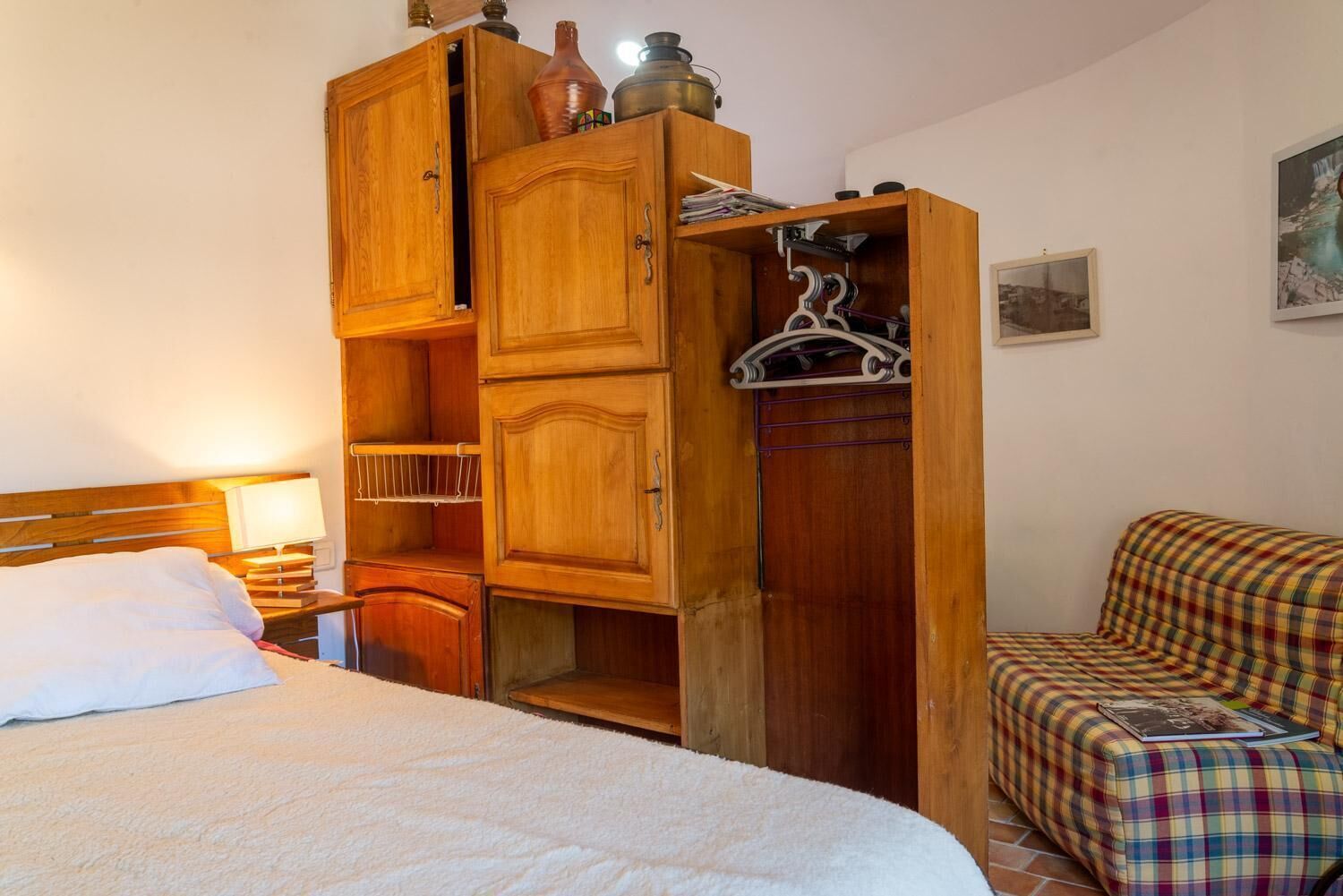 Une chambre à coucher avec un lit, une armoire en bois, un fauteuil à carreaux et un tableau accroché au mur.