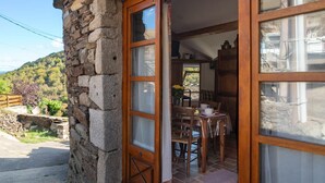 A stone building with a wooden door and windows, a dining area with a table and chairs, and a view of a green landscape.