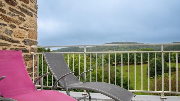 A balcony with two lounge chairs, one pink and one grey, overlooking a green landscape with hills. - Gîte B Les Prés - CHADENET (CHADENET)