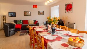 A dining area with a table set for four, a sofa, and a vase with flowers. - Gîte B Les Prés - CHADENET (CHADENET)