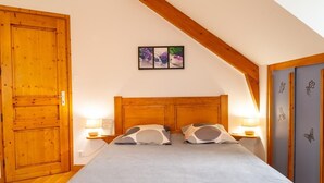 A bedroom with a wooden headboard, two bedside tables with lamps, a bed with grey bedding, a wooden door, and a wall-mounted picture. - Gîte B Les Prés - CHADENET (CHADENET)