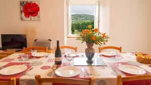 A dining area with a table set for four, a bottle of wine, and a vase of flowers. - Gîte B Les Prés - CHADENET (CHADENET)