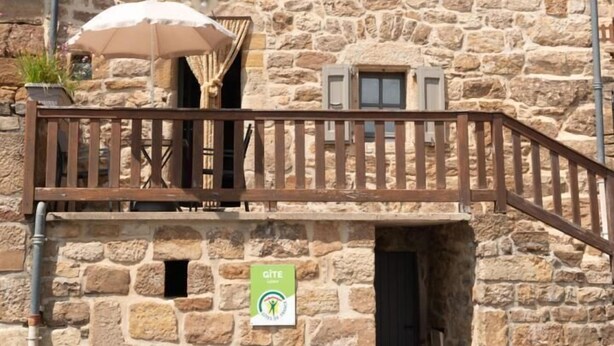 A stone building with a balcony, a sign indicating a GITE, and a small door.