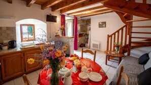 A cozy kitchen with wooden beams, a dining table set with flowers, fruit, and a pitcher.