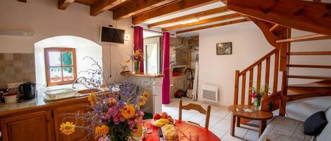Una cocina acogedora con vigas de madera, una mesa de comedor adornada con flores, fruta y una jarra.