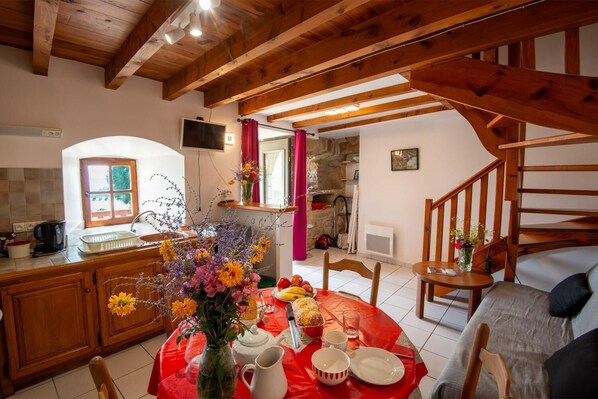A cozy kitchen with wooden beams, a dining table set with flowers, fruit, and a pitcher.
