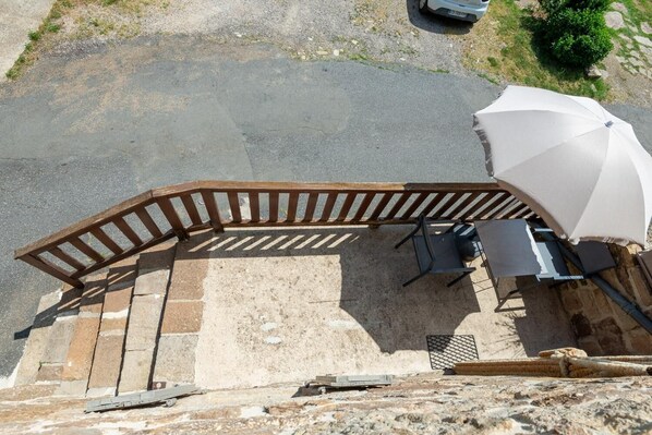 Un patio con una pérgola de madera, asientos exteriores y un paraguas blanco.
