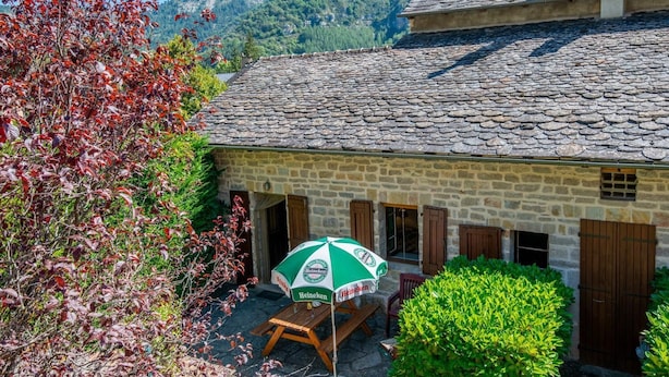 A stone building with a tiled roof, a wooden table, and an umbrella.