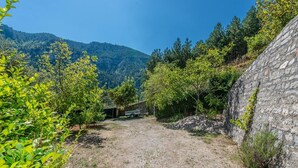 A rural property with a stone wall, a small building, and a dirt path surrounded by greenery and hills.