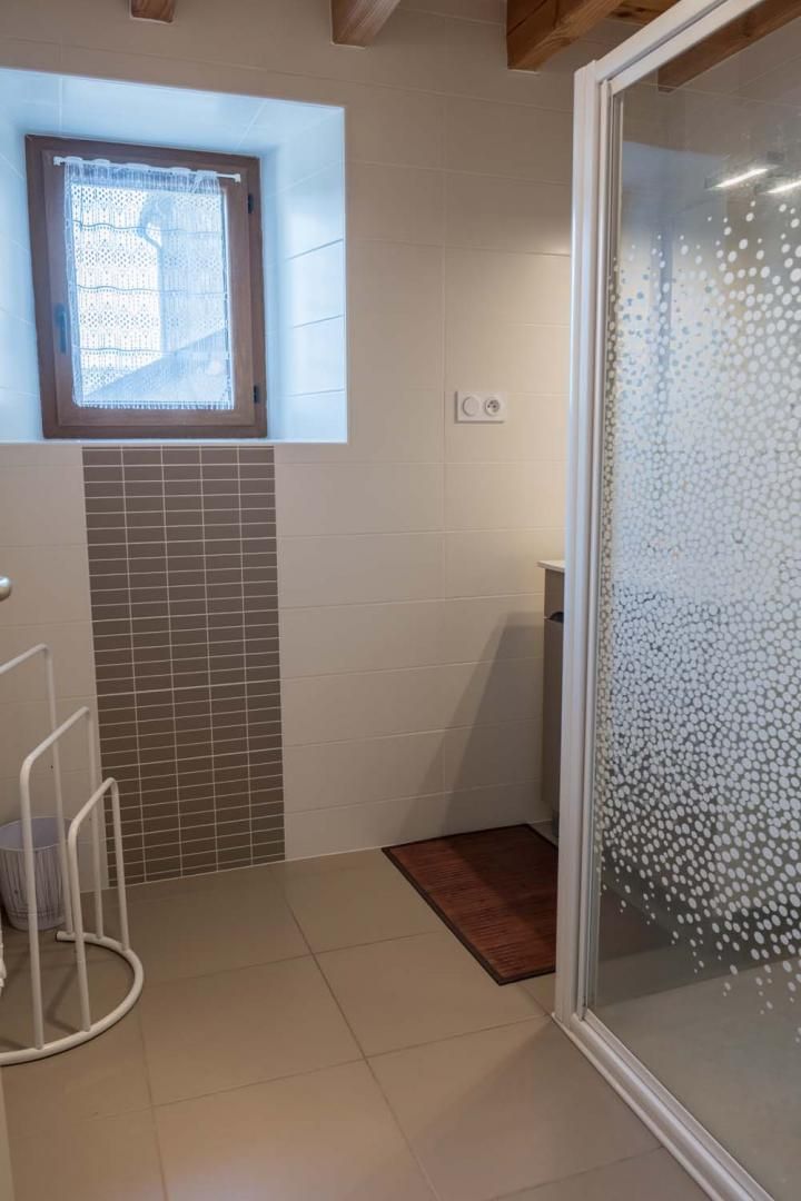 A bathroom with a shower, a window, and a tiled floor.