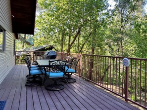 Eine Holzterrasse mit Tisch und Stühlen, umgeben von einem Metallgeländer und Bäumen.