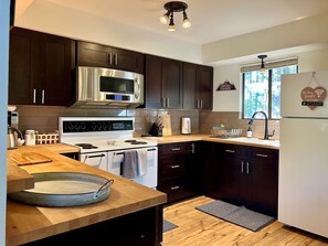 A modern kitchen with dark cabinetry, stainless steel appliances, and a wooden countertop. - Creekside Chalet - Prescott Cabin Rentals (Prescott)