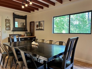 Un espace repas comprenant une grande table, des chaises, un plafond en bois et une fenêtre donnant sur la forêt.