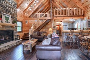 A log cabin interior with a fireplace, a staircase, a dining area, and a kitchen.