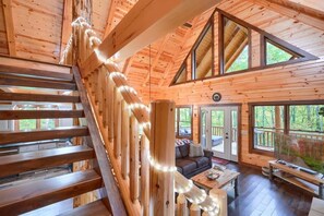 A wooden cabin interior with a staircase, a living area with a sofa and coffee table, and large windows.