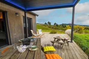 En træterrasse med udendørs møbler, herunder et bord og stole, med udsigt over et smukt landskab.