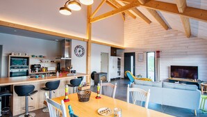 Ein geräumiges Wohnzimmer mit Holzbalkendecke, eine Küche mit modernen Geräten und ein Essbereich mit Tisch für zwei Personen.