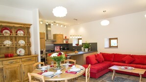 Ein gemütlicher Wohnraum mit Essbereich, einem roten Sofa, einer Küche und einem für vier Personen gedecktem Esstisch.